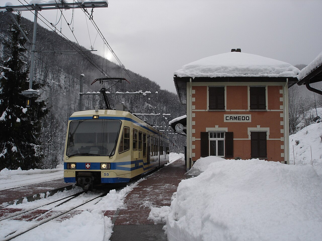Yellow-and-blue Centovalli train beside snow-covered Camedo station