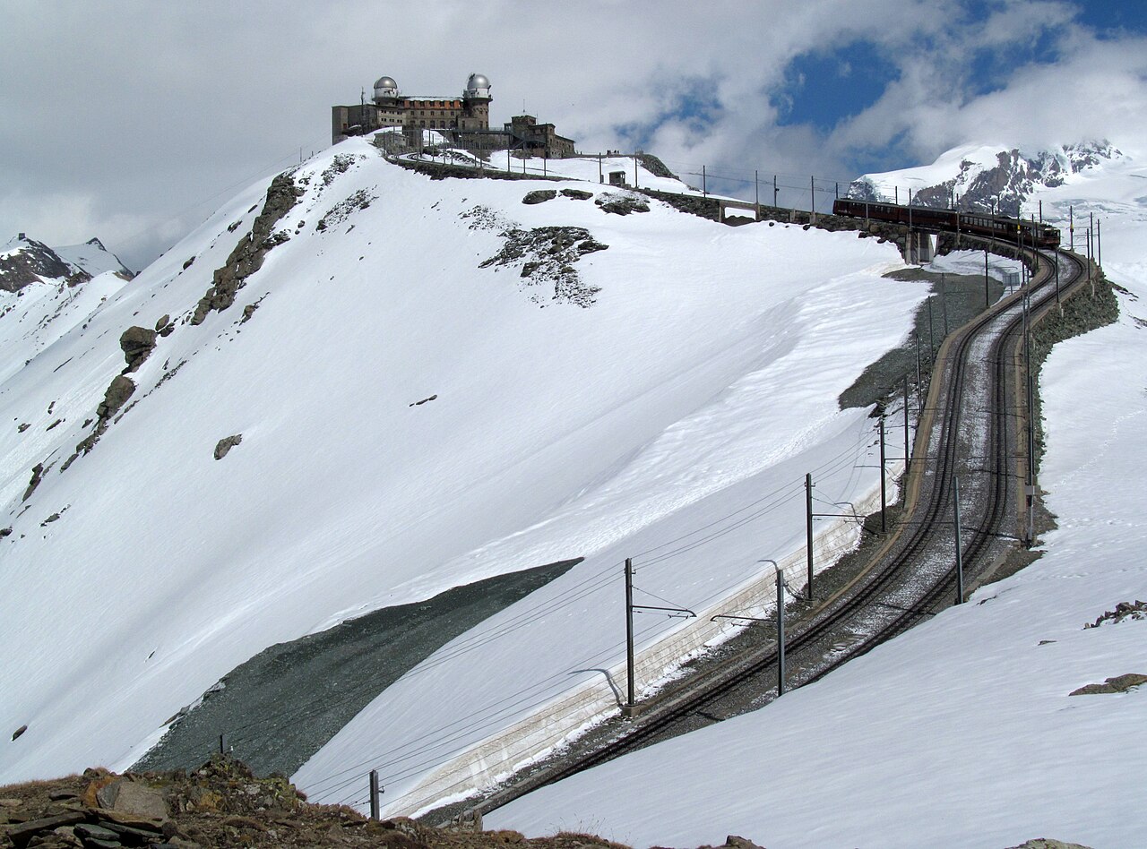 Gornergrat Railway train and curved tracks below the snowy mountain summit