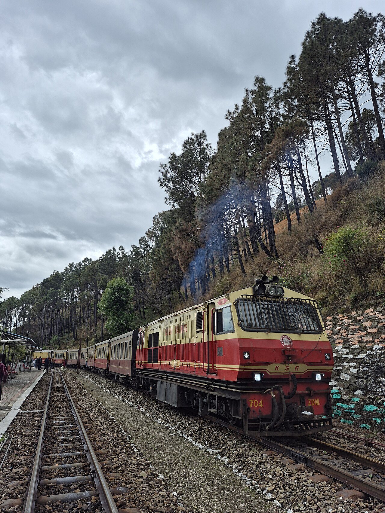 Red-and-cream Kalka Shimla locomotive and passenger cars beneath tall pine trees