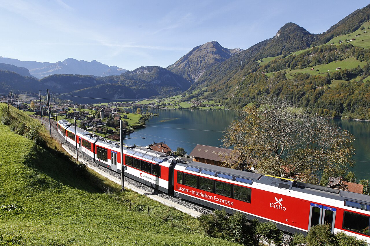Red-and-white Luzern Interlaken Express on a hillside above blue Lake Lungern